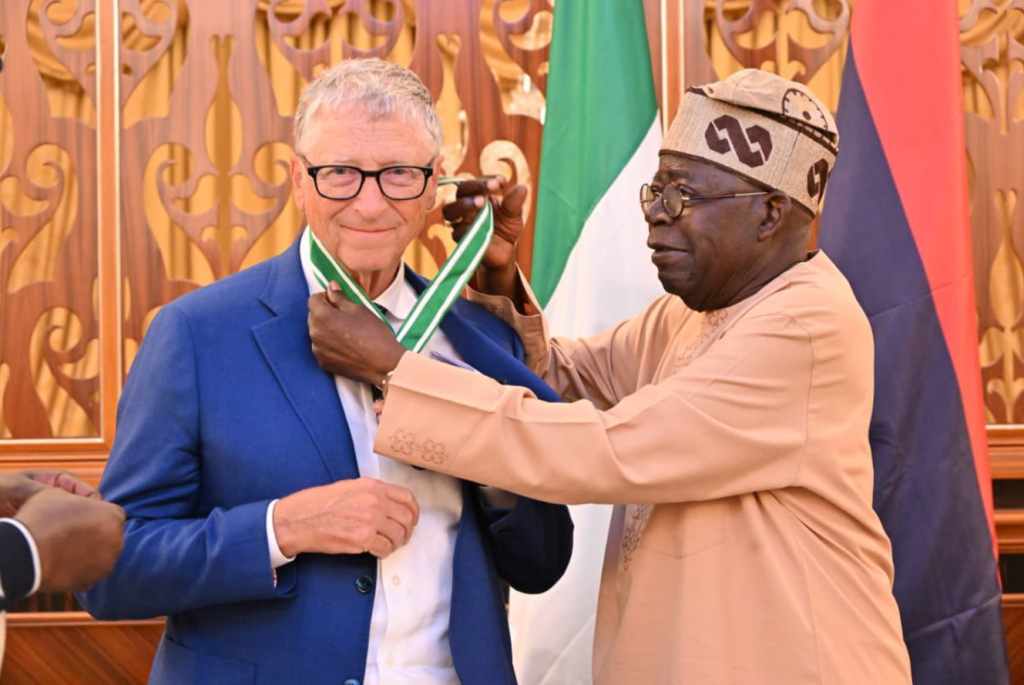 Bill Gates standing left and President of Nigeria Tinubu putting medal around his neck
